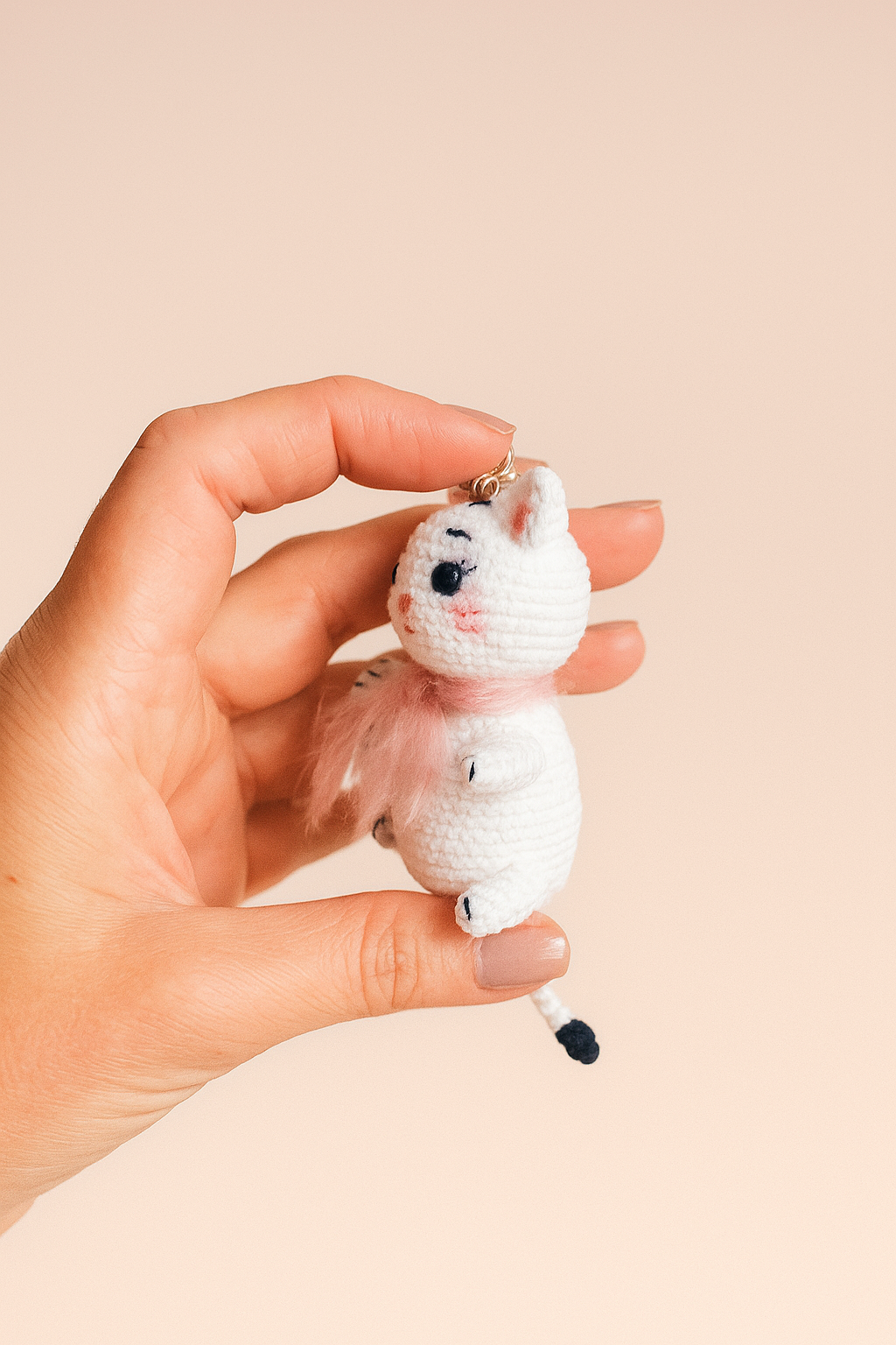 A small white crochet cat keychain with a pink scarf, handmade in amigurumi style
